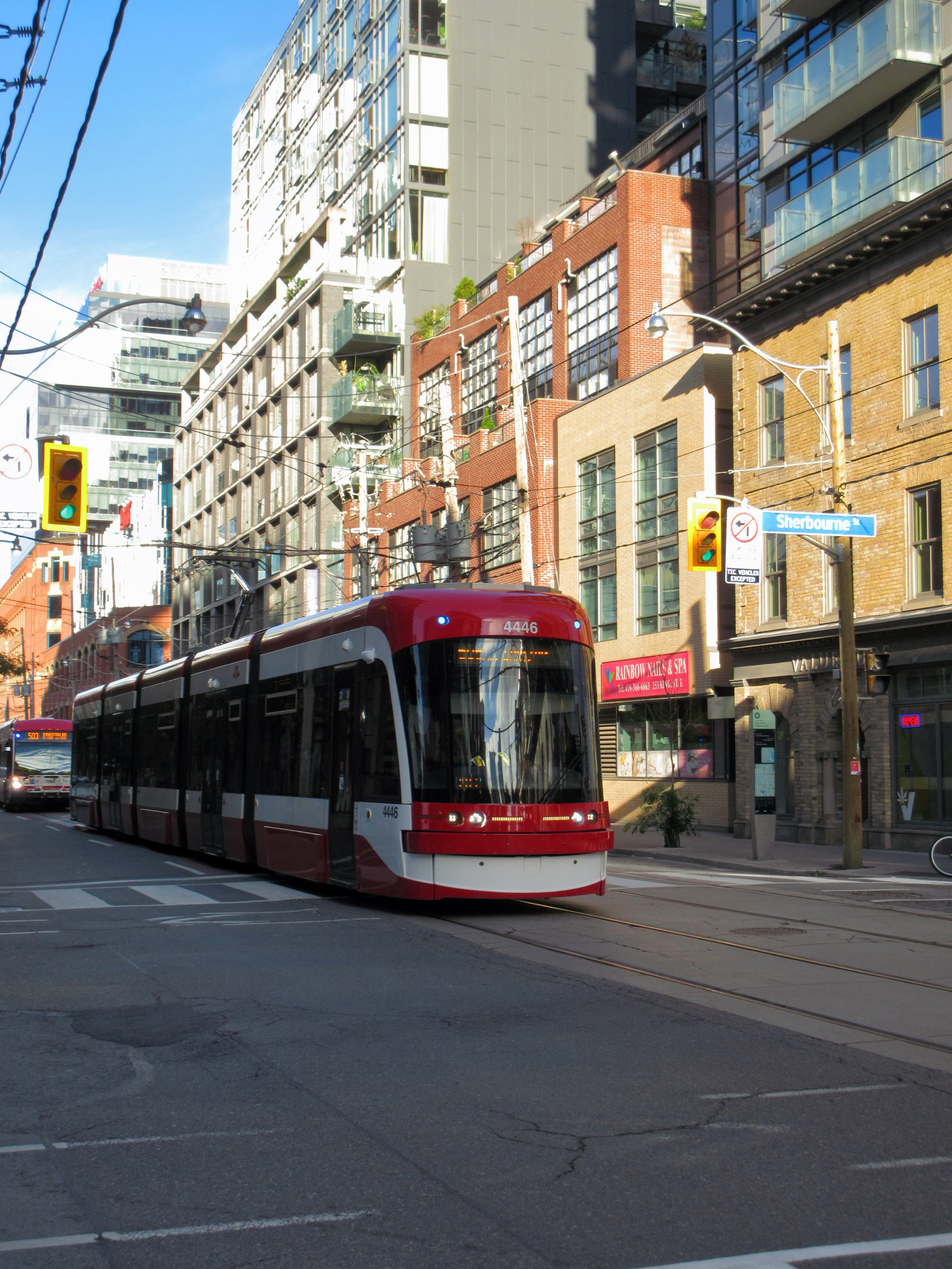 A red and white Toronto streetcar crossing an intersection, with brick storefronts and glass condo towers behind it