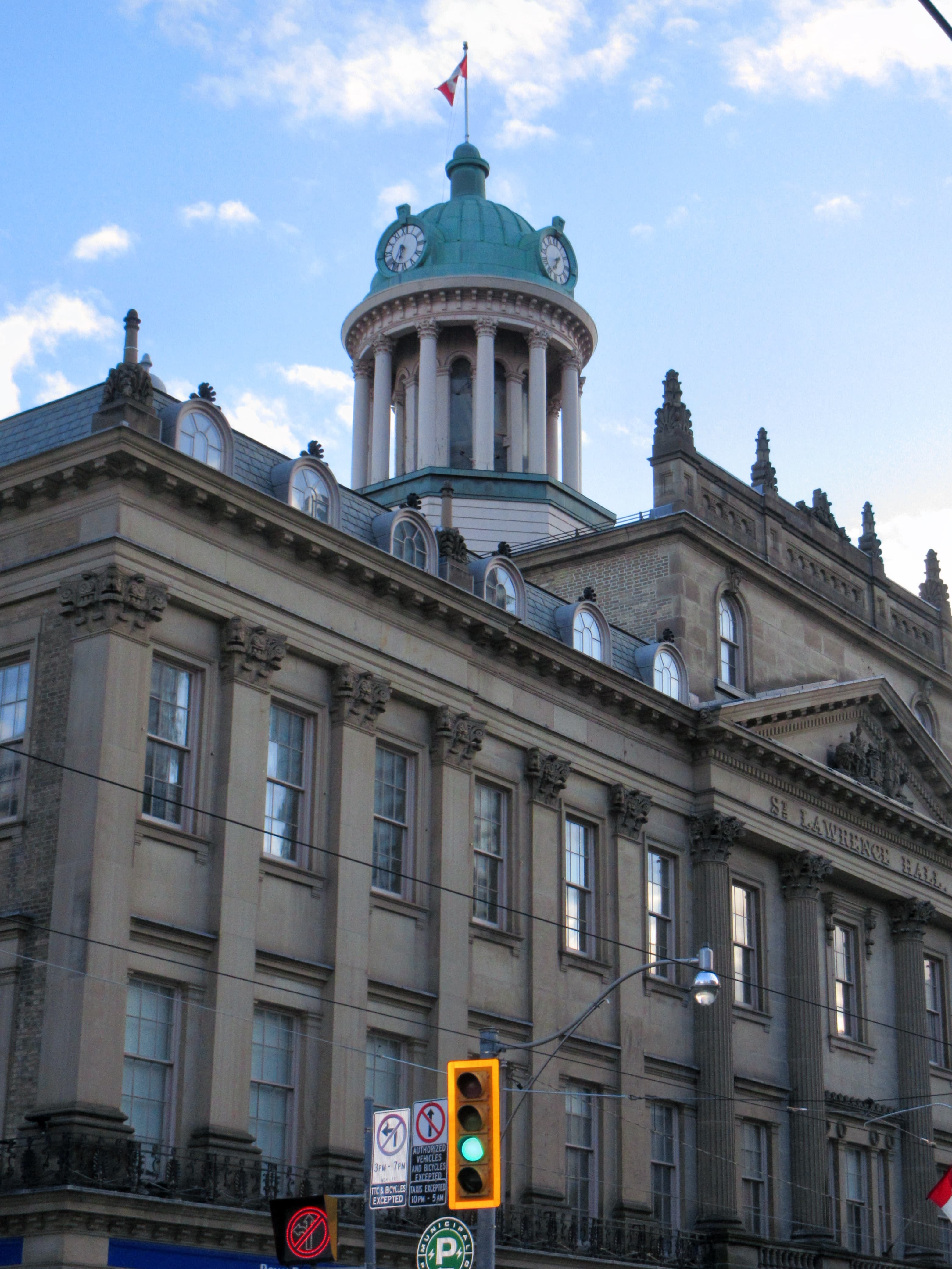 A historic stone building with a green copper dome and clock tower against a partly cloudy blue sky