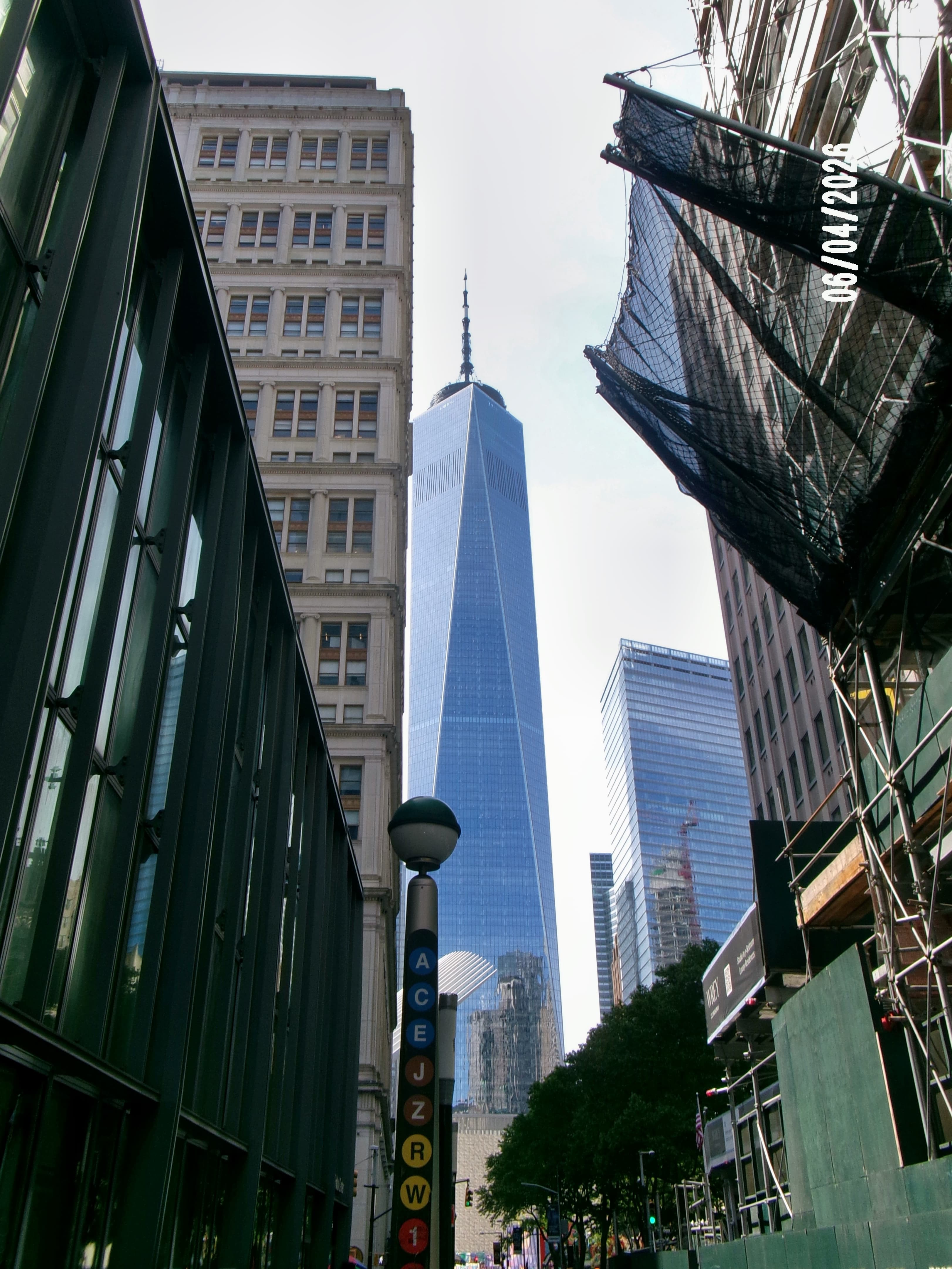 One World Trade Center rising between dark glass buildings, seen from street level looking up